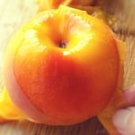 Peeling a peach with fingers on a wooden surface.
