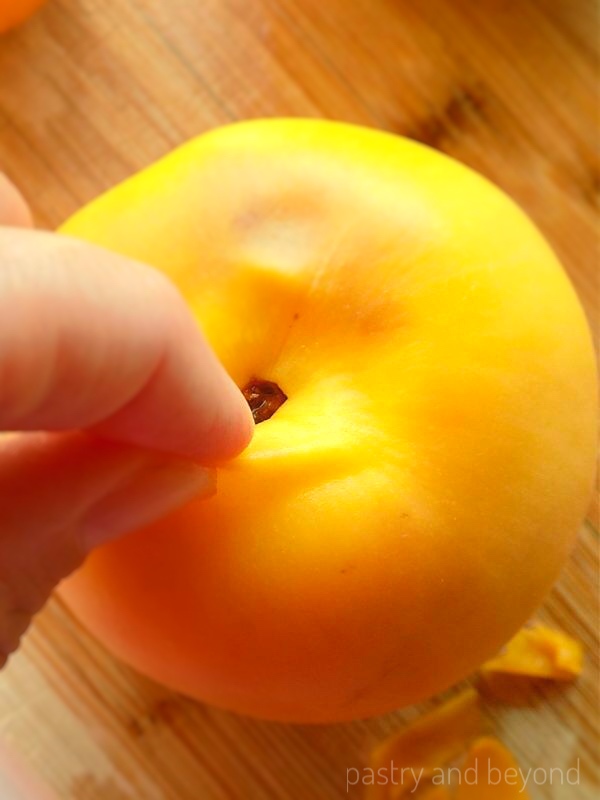 Pulling a small part of the peach's skin with fingers from the top.