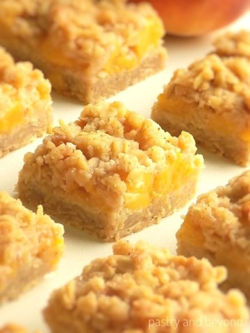 Peach crumb bars in a row on a white surface.