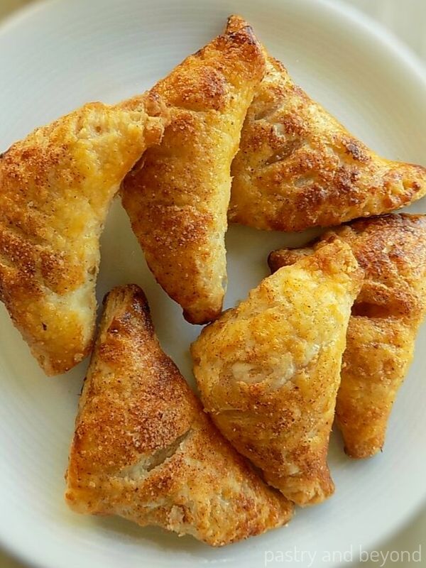 Six small apple turnovers on a white plate.