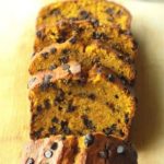 Chocolate chip pumpkin bread slices on a wooden chopping board with pumpkins in the background.