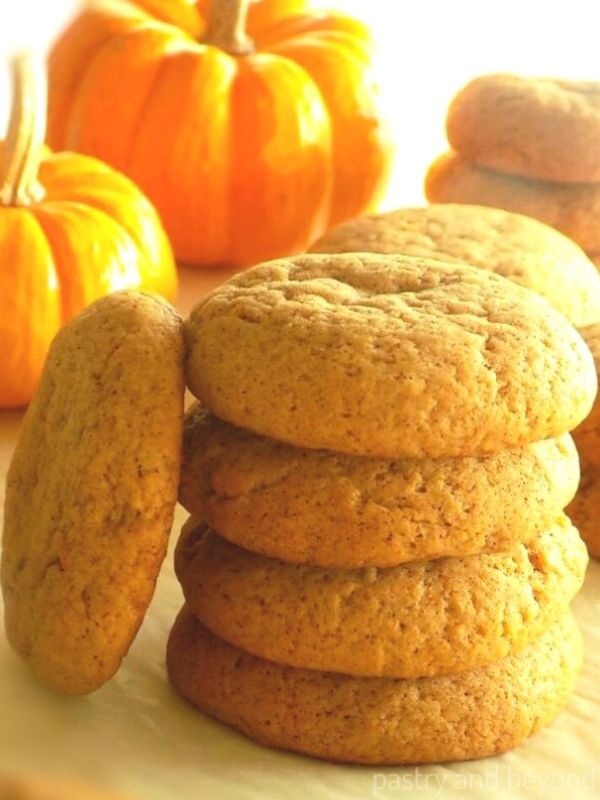 Stacked soft pumpkin cookies and pumpkins in the background.