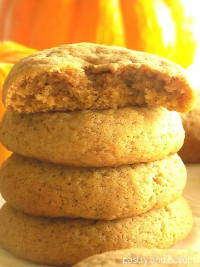 Stacked pumpkin spice cookies, the one on top is in half and pumpkin in the background.
