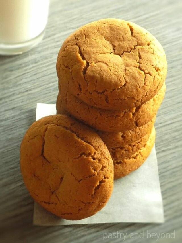 Stacked ginger molasses cookies, glass of milk in the background.