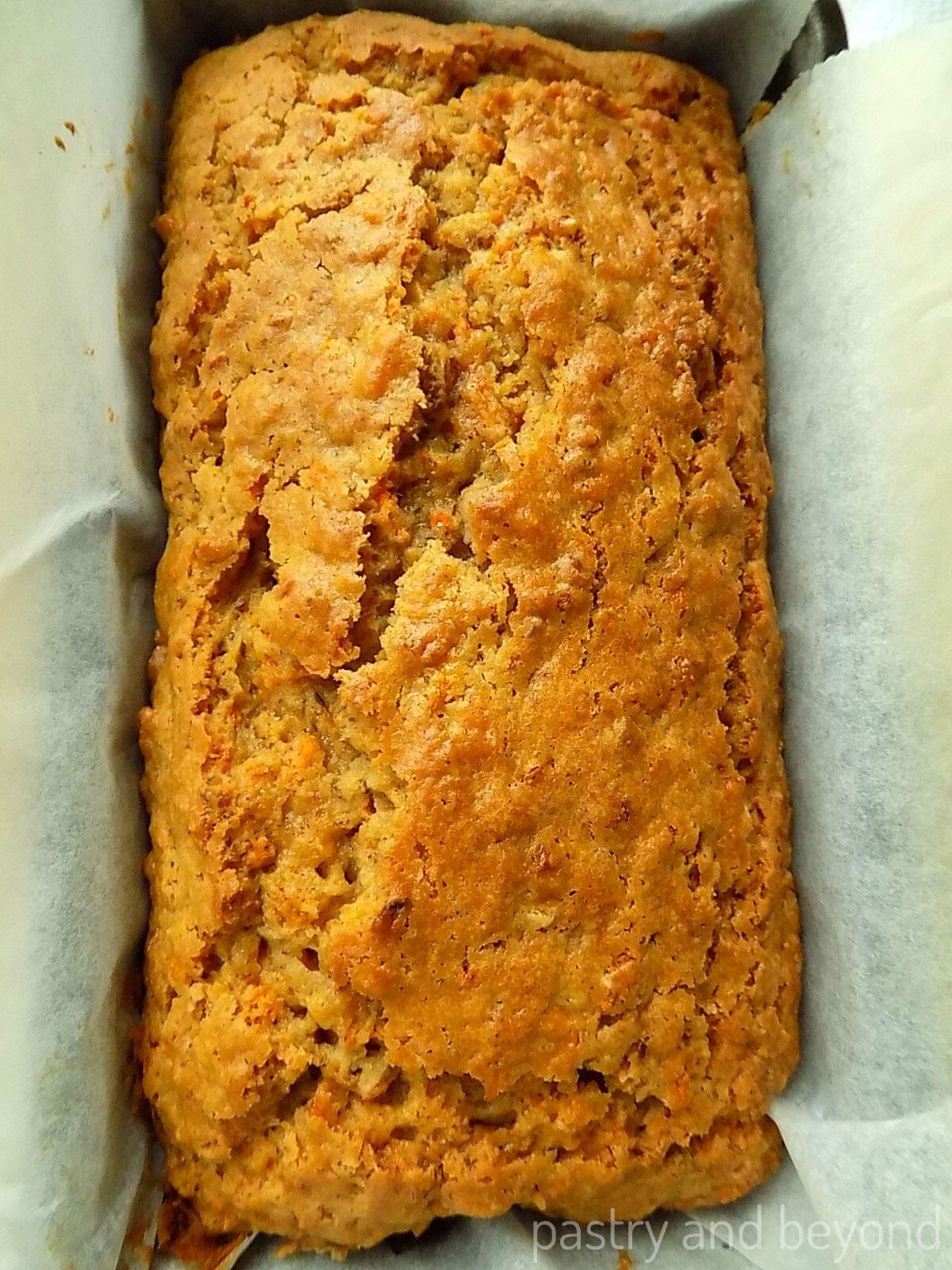 Carrot cake in a loaf pan that is covered with parchment paper.