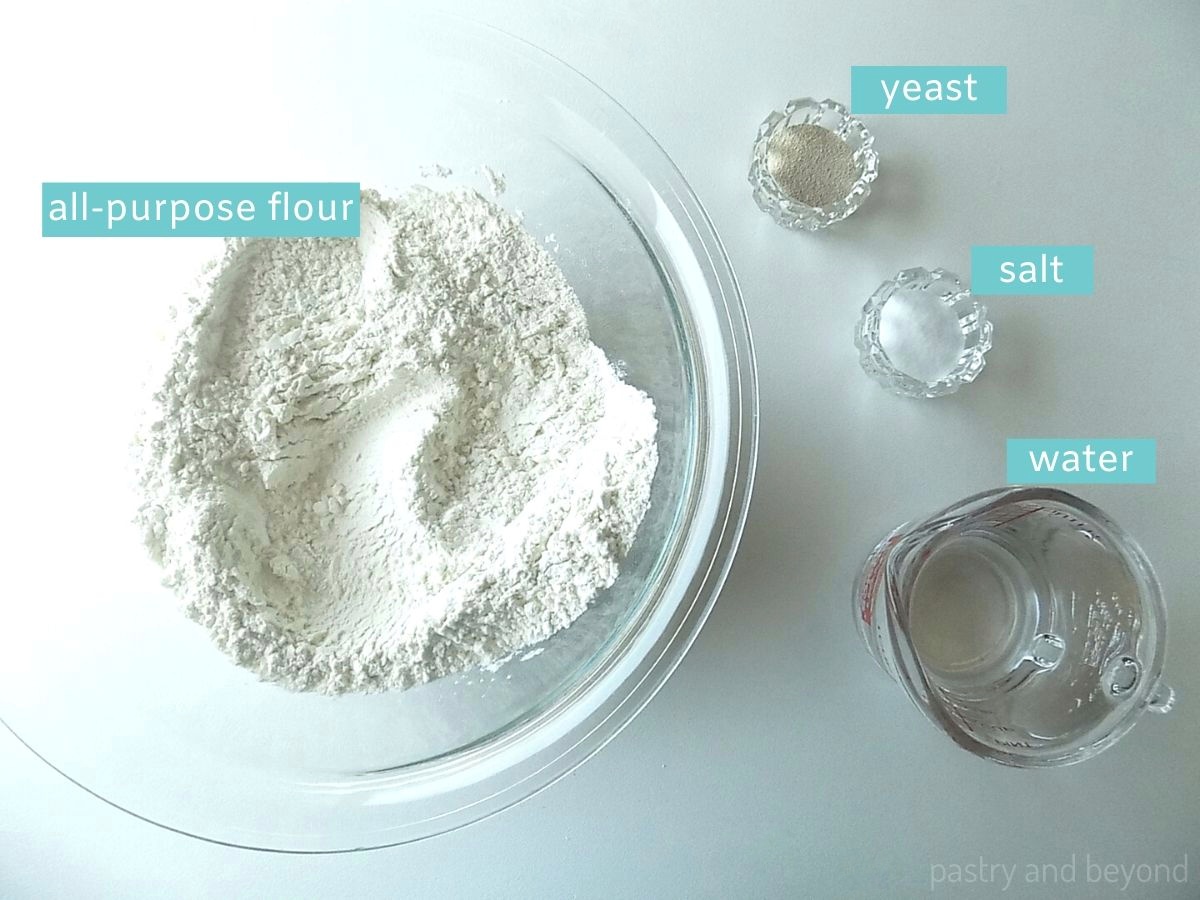 White bread ingredients; flour, salt, instant yeast and water on white surface.