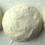Pizza dough that is made by hand and rolled into a ball on a floured surface.