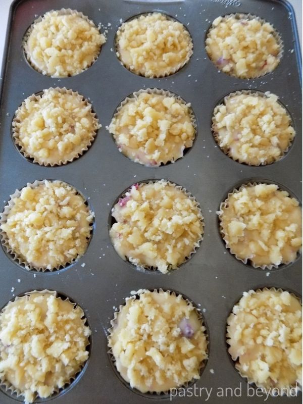 Raspberry muffin batter with crumble dough in a muffin tin.