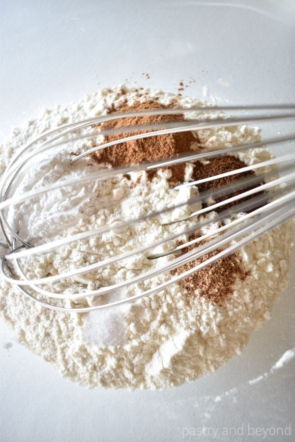 Flour, baking powder, cinnamon, cloves, nutmeg and salt in a bowl with a whisk.