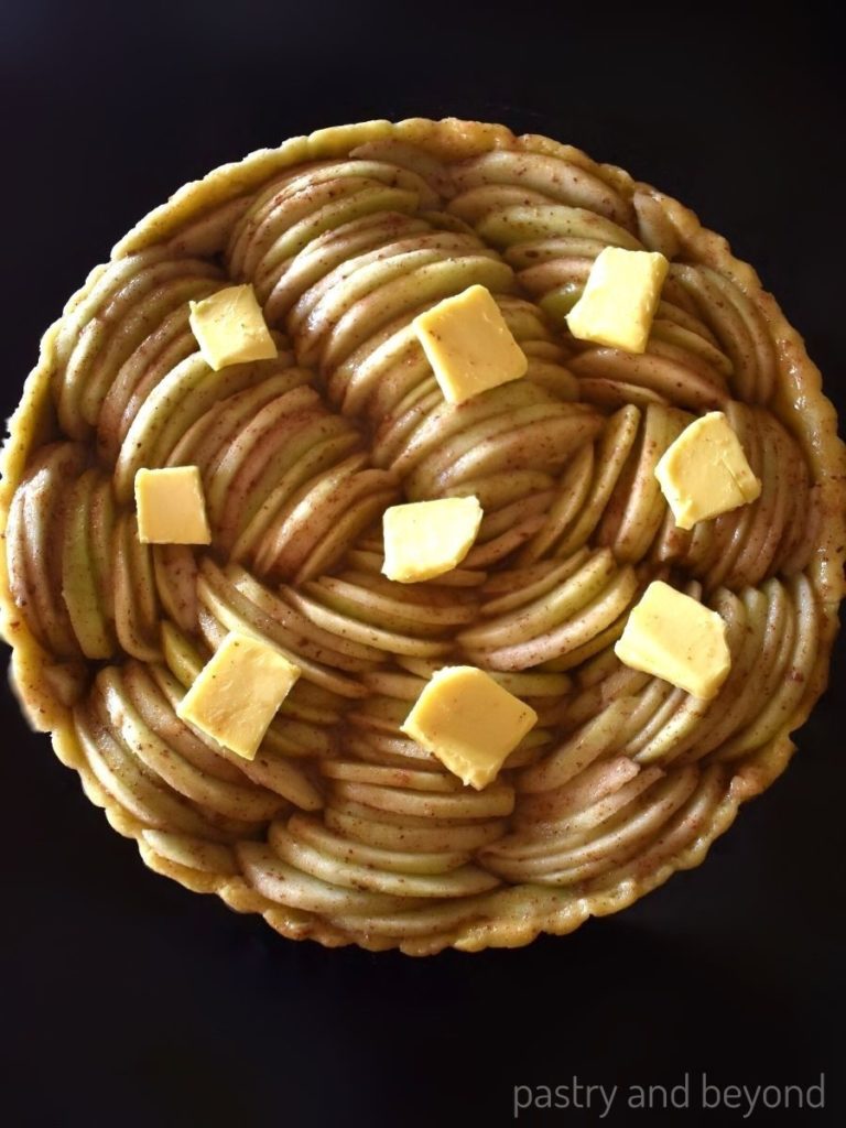 Apple slices with butter on top on unbaked tart crust in a pan.