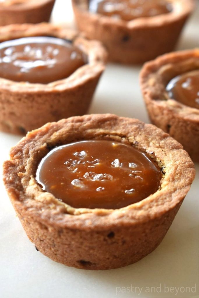 Caramel filled chocolate chip cookie cups on a white surface.