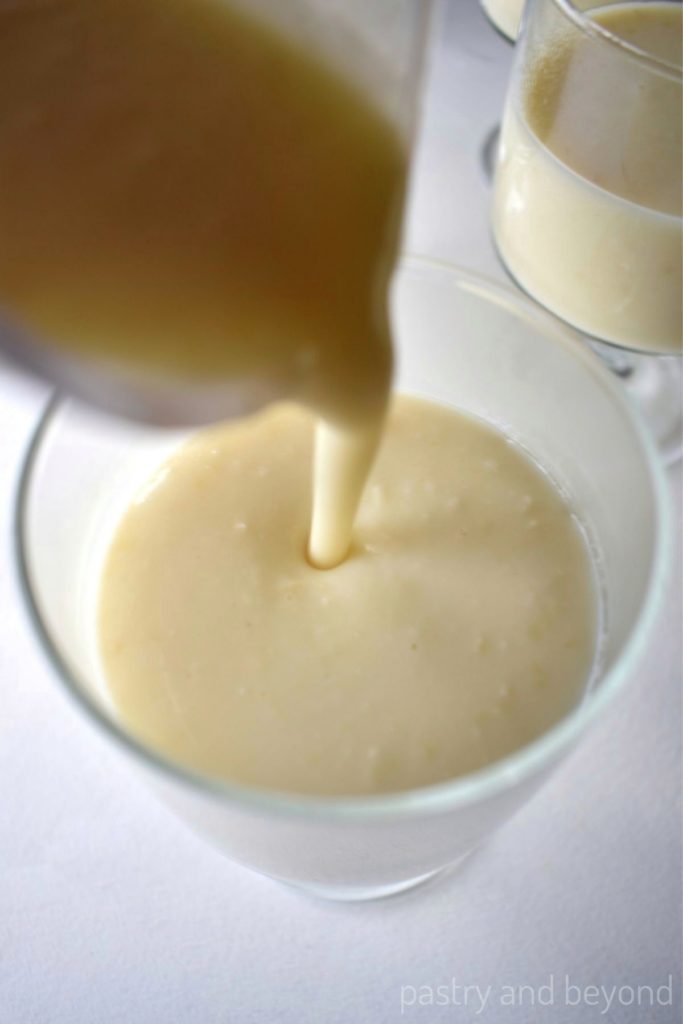 Pouring almond pudding from a jug into a serving glass.