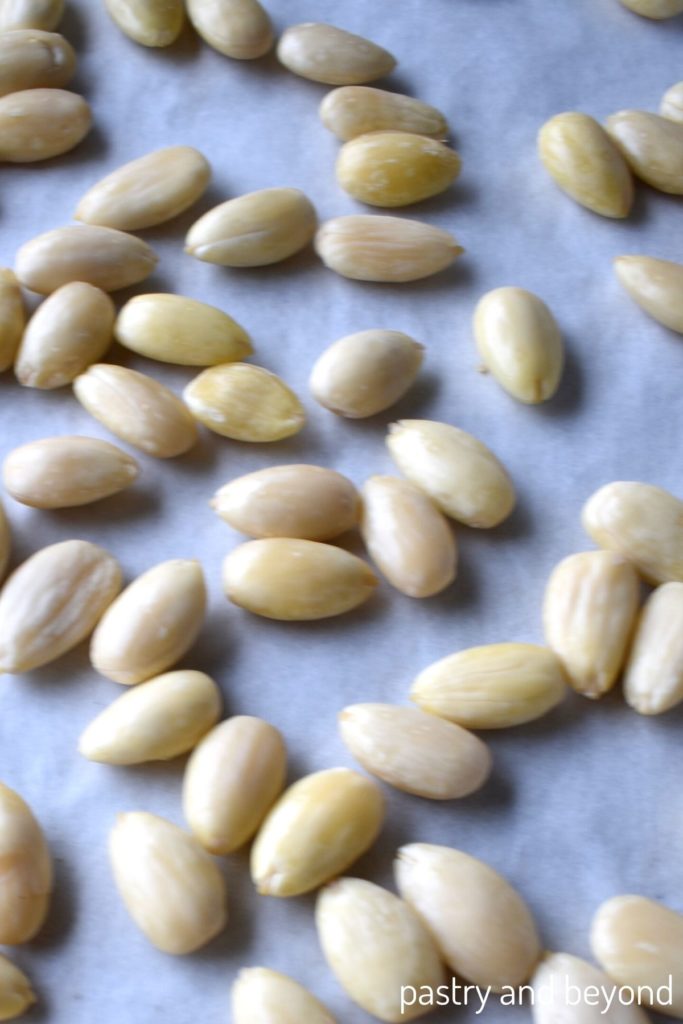 Blanched almonds on a parchment paper lined baking sheet.