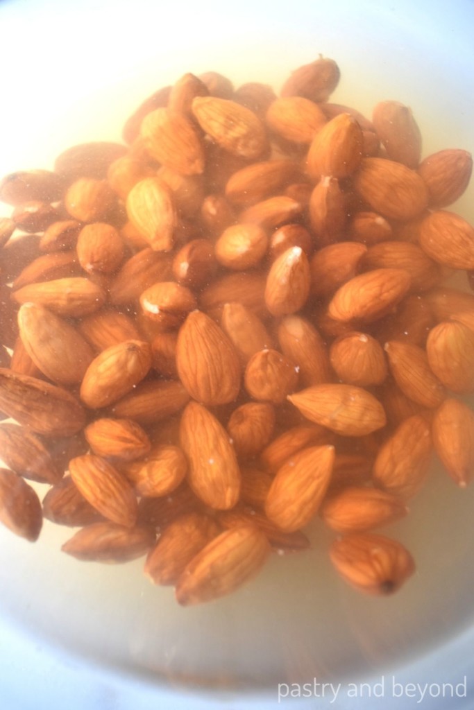 Raw almonds covered with water in a glass bowl to blanch the almonds.