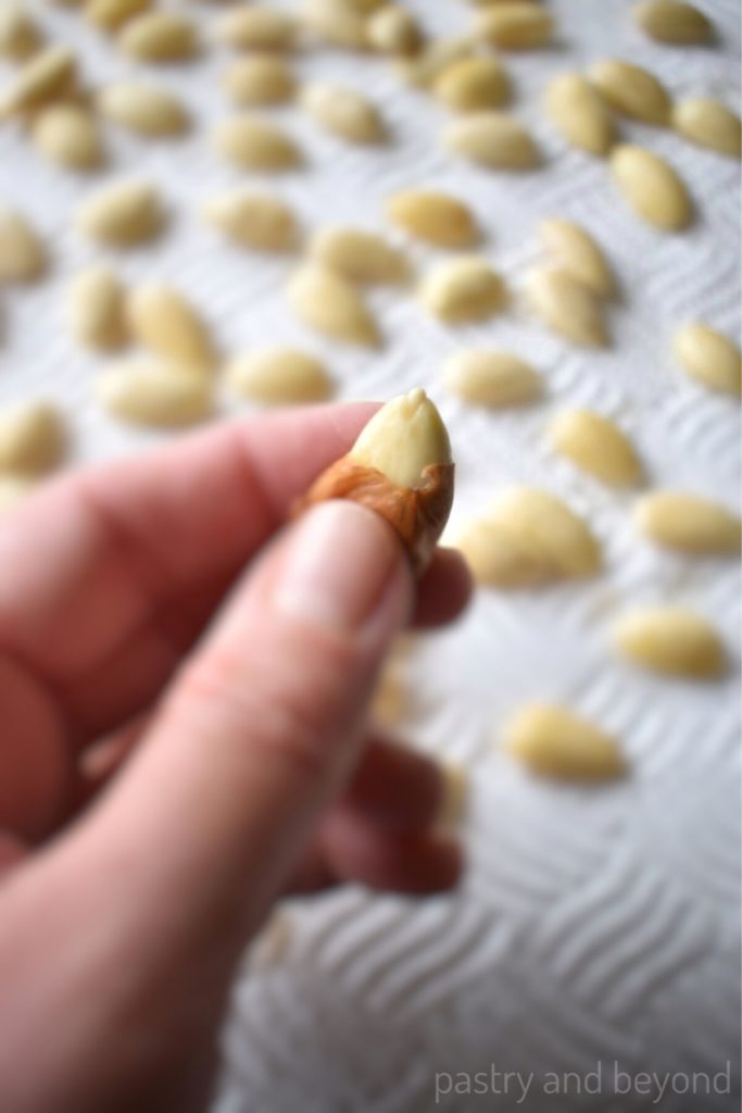 Squeezing the almond with thumb and forefinger to peel the almond. 