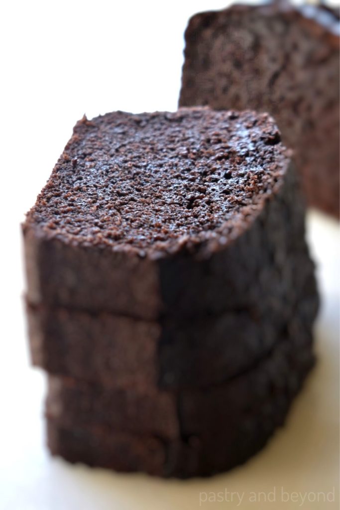 Stacked chocolate cake loaf slices on a white surface.