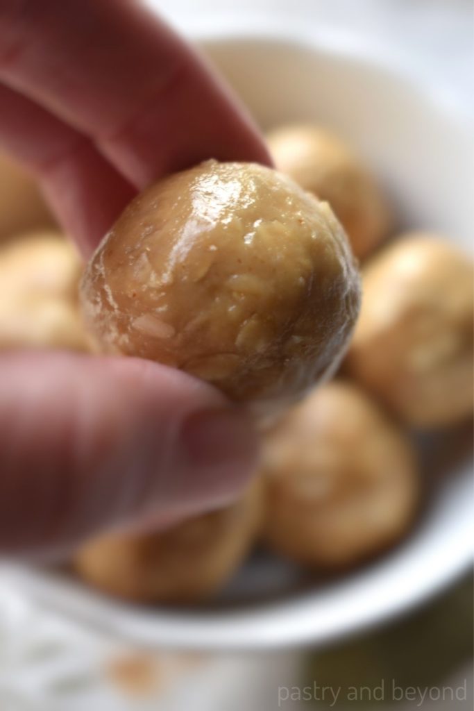 A hand holding peanut butter balls above a bowl.
