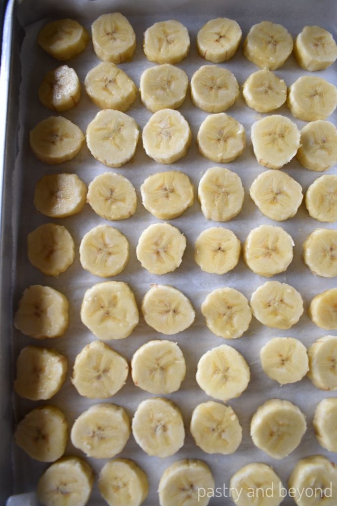 Sliced bananas on a parchment paper lined small baking sheet.