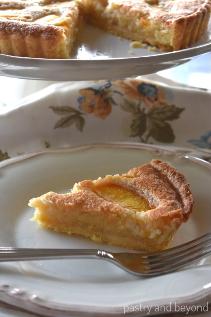 Peach almond tart on a plate and serving plate with tart in the background.