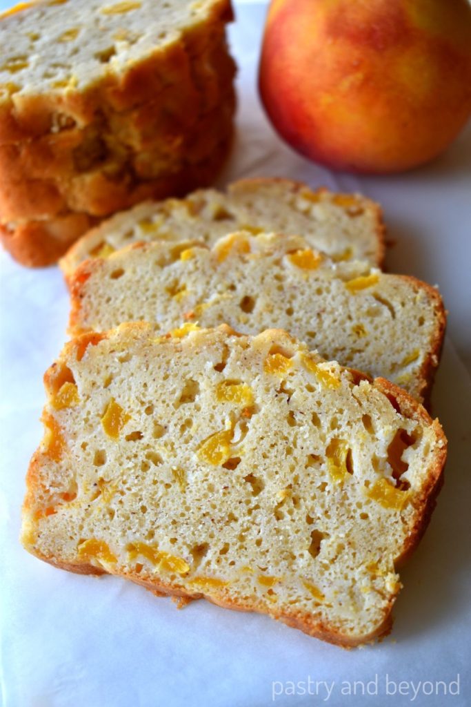 Slices of peach bread with stacked slices and peach in the background.