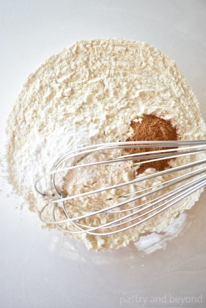 Flour, cinnamon and baking powder with a whisk in a bowl.