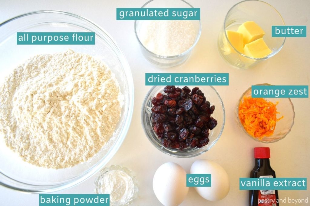 Ingredients of cranberry orange biscotti on a white surface.