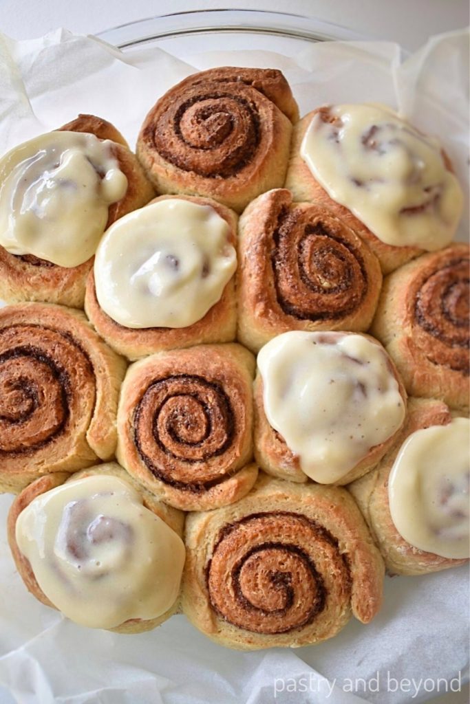 Cinnamon rolls in a round glass dish with some of them iced on top.