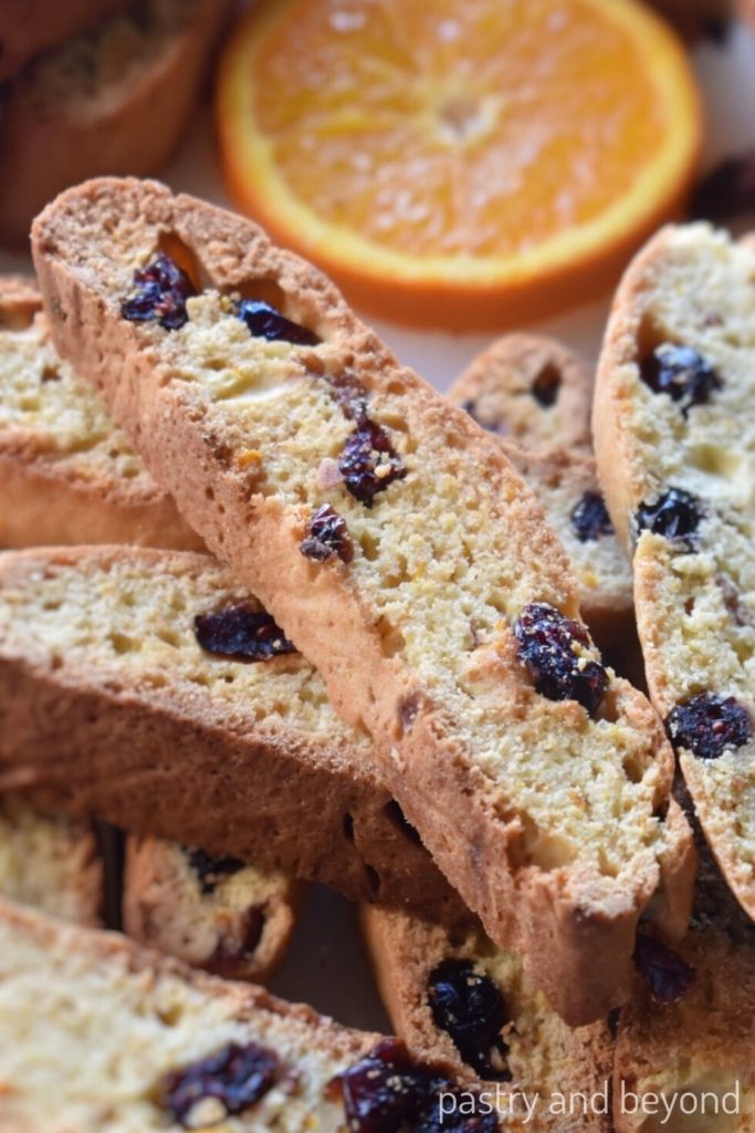 Orange cranberry biscotti slices with a slice of orange in the background.