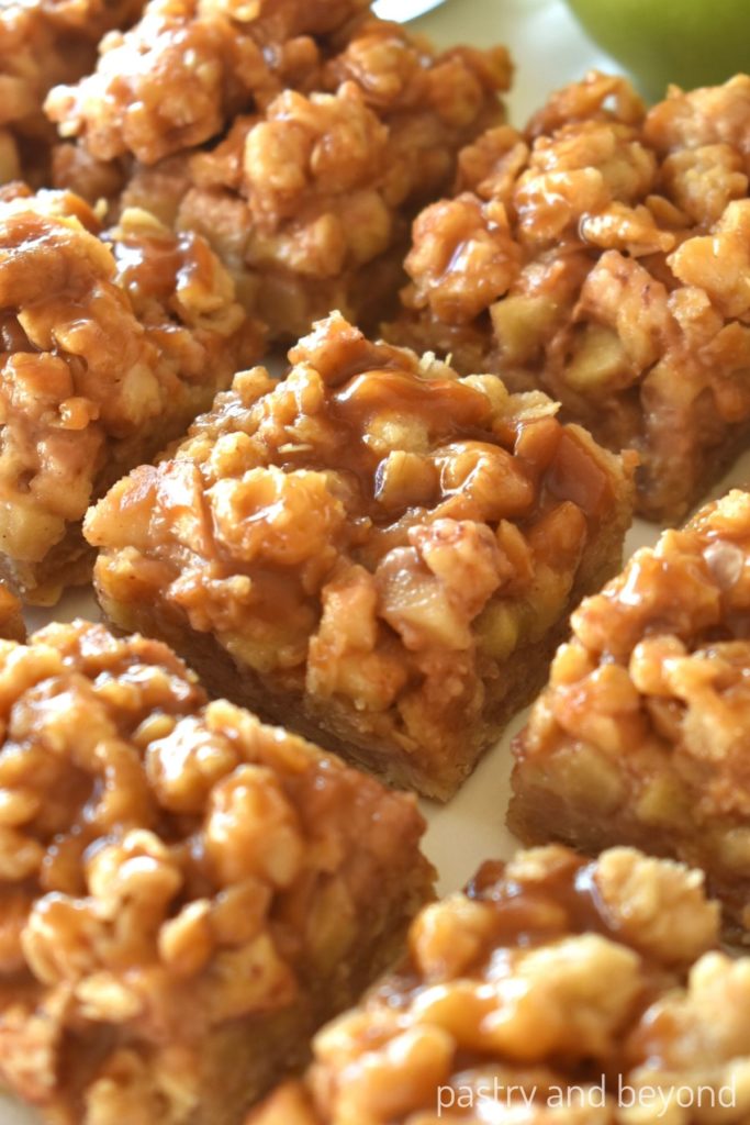Apple oatmeal bars with caramel sauce on top with an apple in the background.