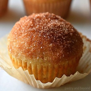 Cinnamon sugar muffin on a white surface with other muffins in the background.