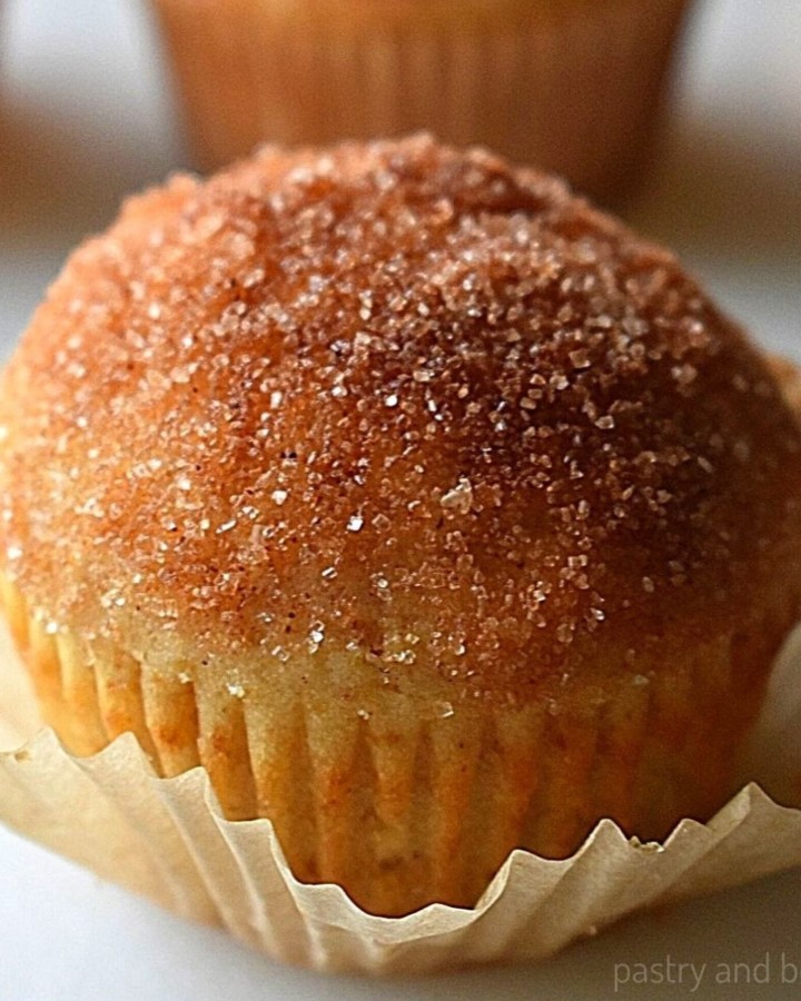 Cinnamon sugar muffin on a white surface with other muffins in the background.