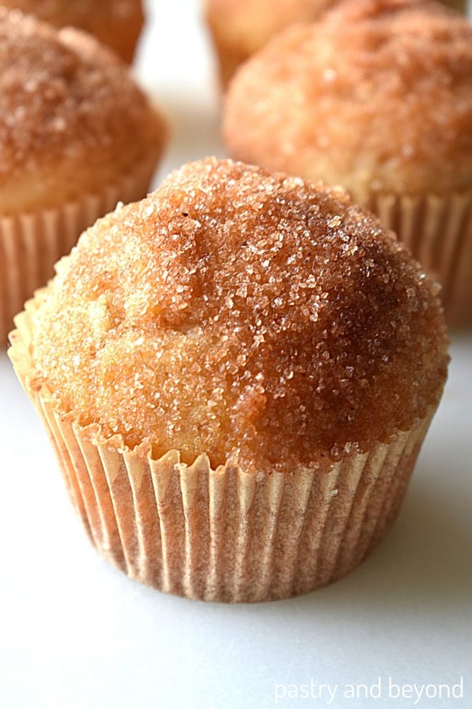 Muffins with cinnamon sugar topping on a white surface.