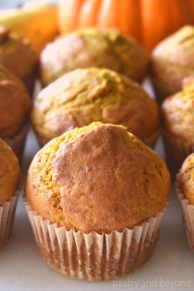 Pumpkin banana muffins on a white surface with banana and pumkin in the background.