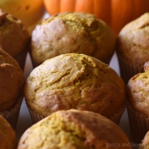 Pumpkin banana muffins with banana and pumpkin in the background.