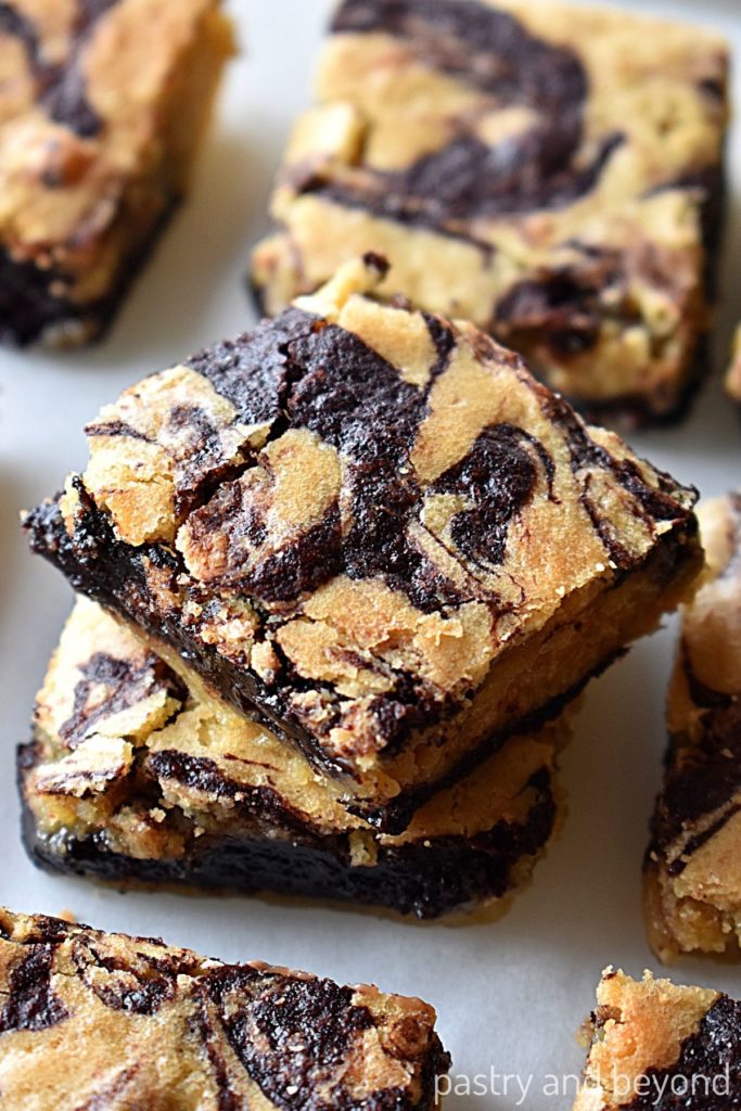 Stacked brownie blondies with other bars on a white surface.