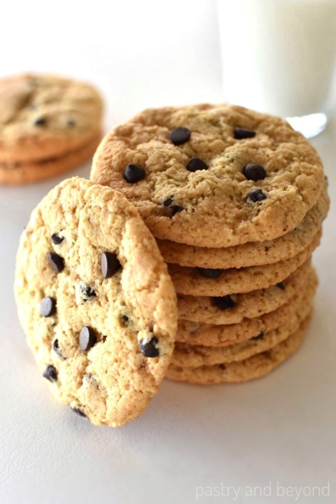 Stacked gluten free chocolate chip cookies with a glass of milk in the background .