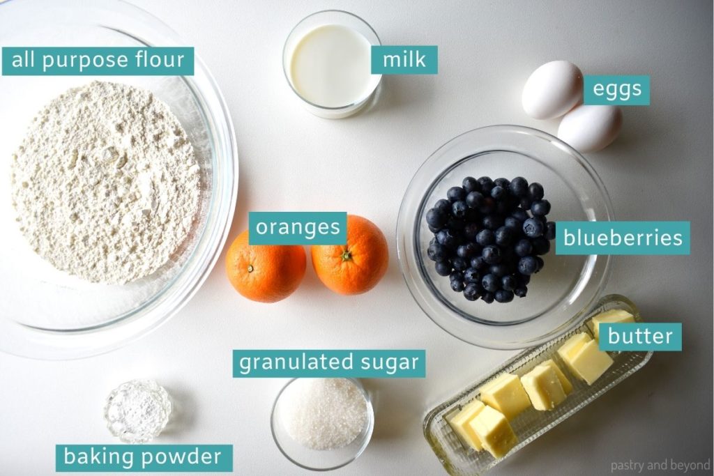 Ingredients of orange blueberry muffins on a white surface.