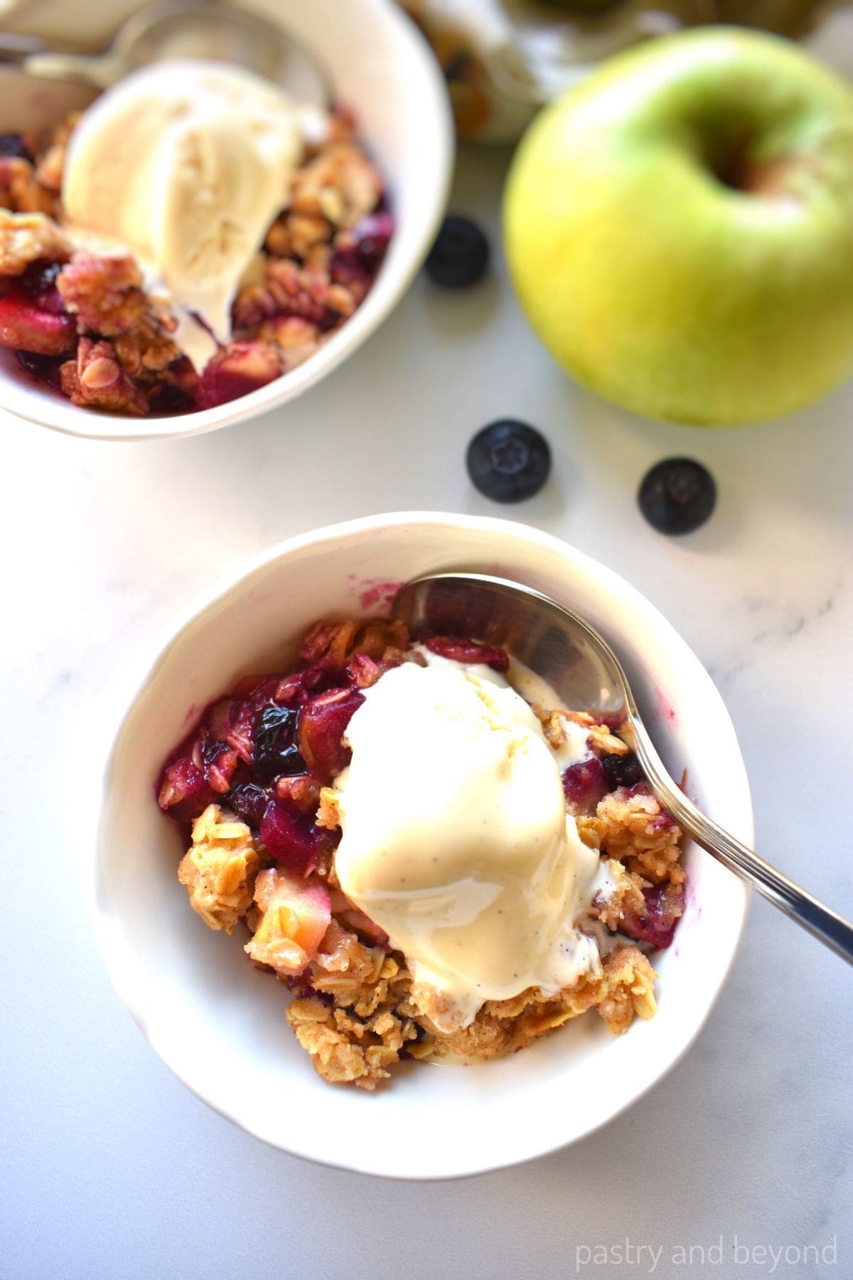 Apple blueberry crumble in small bowls with ice cream on top.