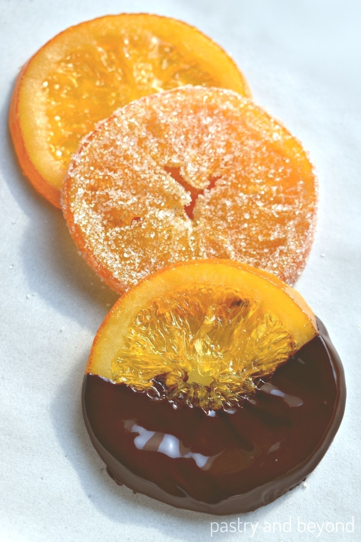 Chocolate covered candied orange, sugar covered candied orange and plain candied orange on a white surface.