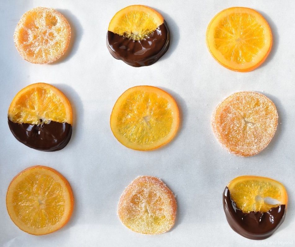 Candied orange slices on a parchment paper; plain, dipped into chocolate and sugar coated.