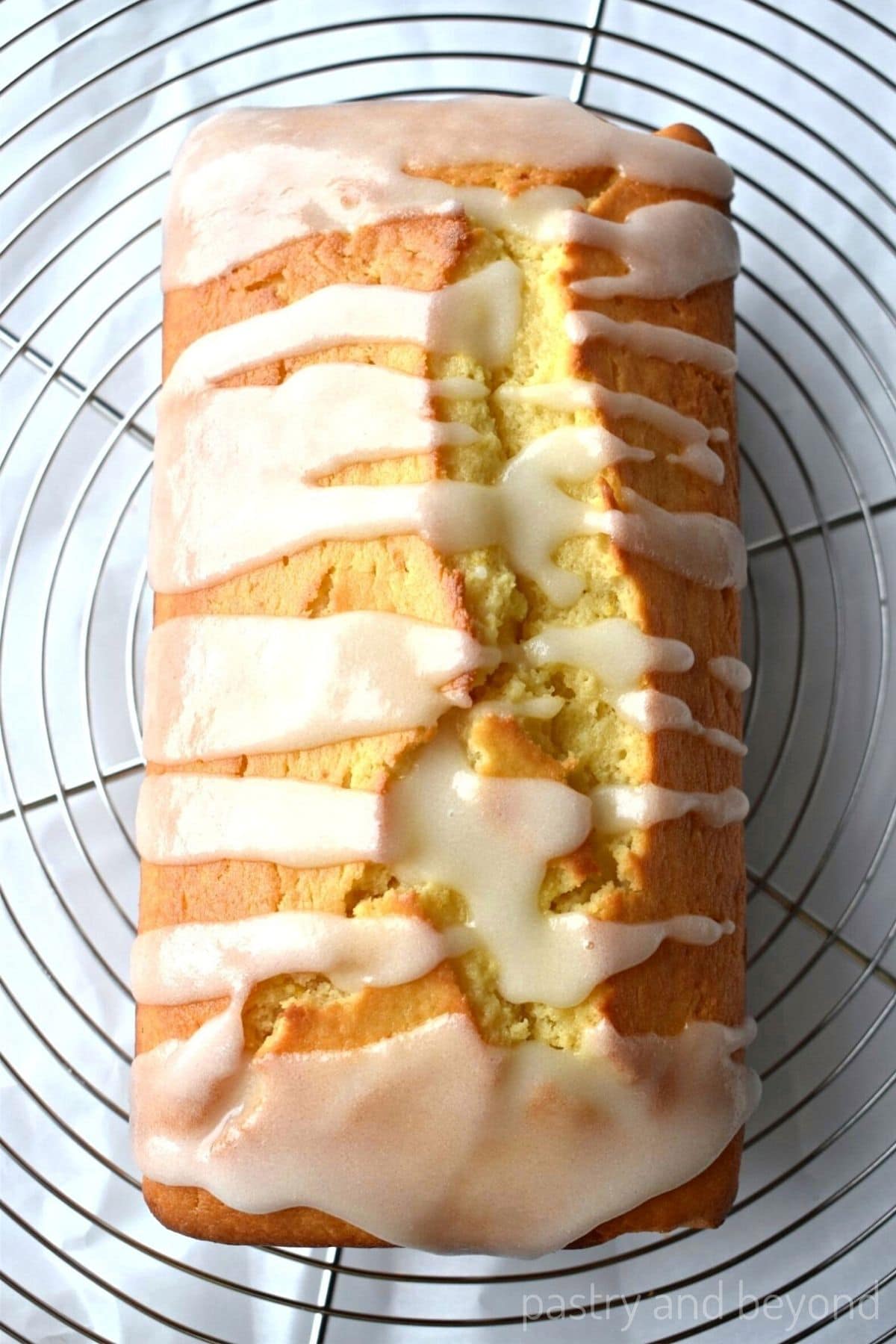 Lemon loaf on a wire rack after lemon glaze poured on top with parchment paper underneath.