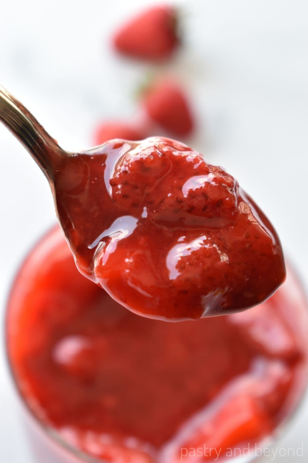 Strawberry sauce on a spoon over a jar.