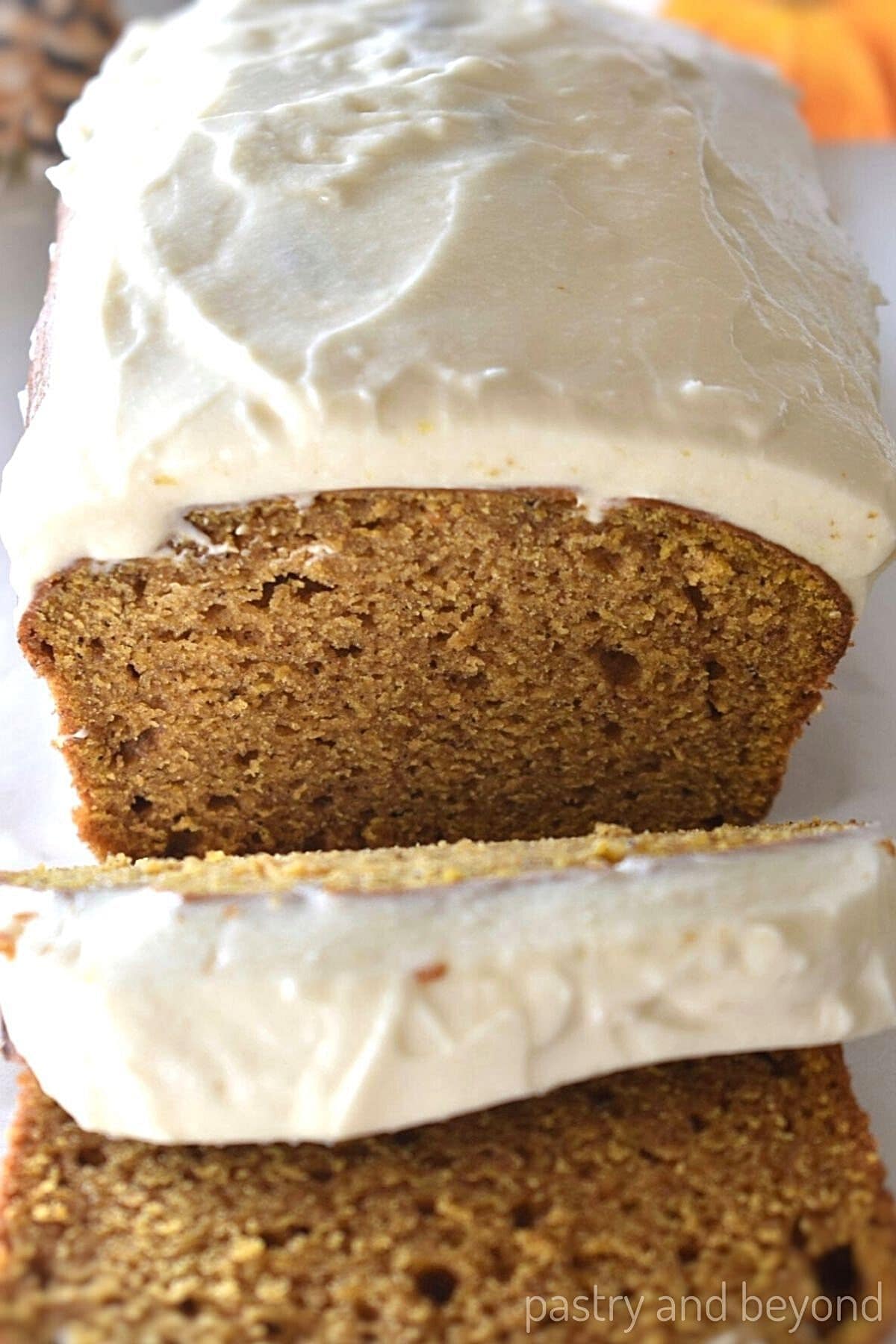 Cream cheese frosted pumpkin loaf with slices.
