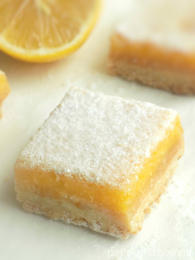 Lemon bars on a white surface with lemon in the background.
